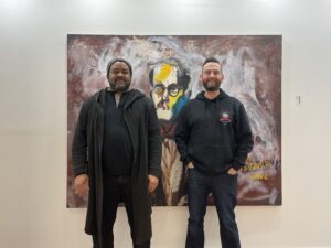 Grey Box Gallery owners Charles Hooper and Rob Stephenson (on theright) pose in front of “Sigmund Freud Visiting the Lascaux Cave,” a 1962 work by Israeli-born artist Eran Shakine.