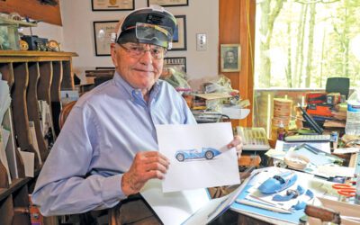 Bob Lutz in his workshop holding a picture of a car.