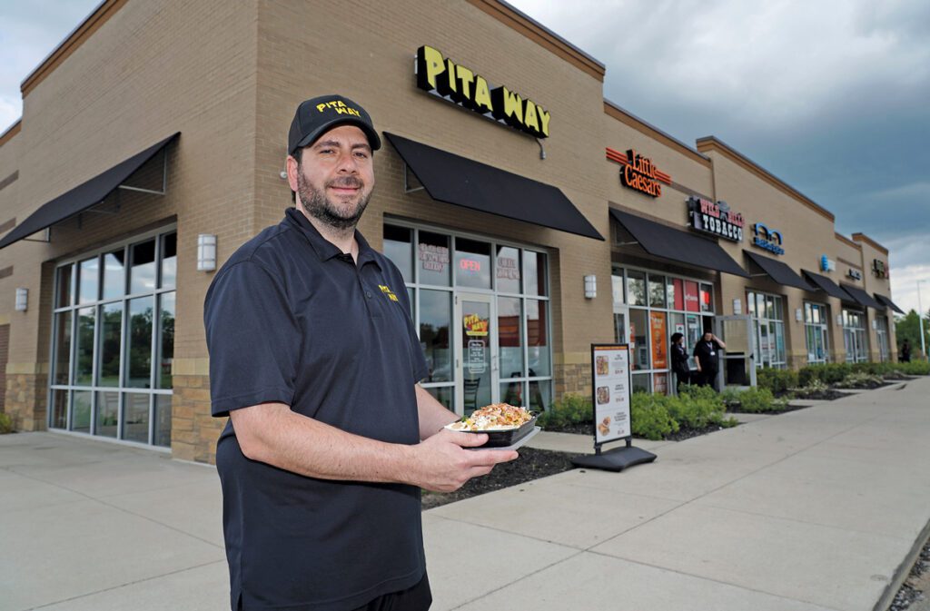 Alex Putrus standing outside of Pita Way holding a sandwich.