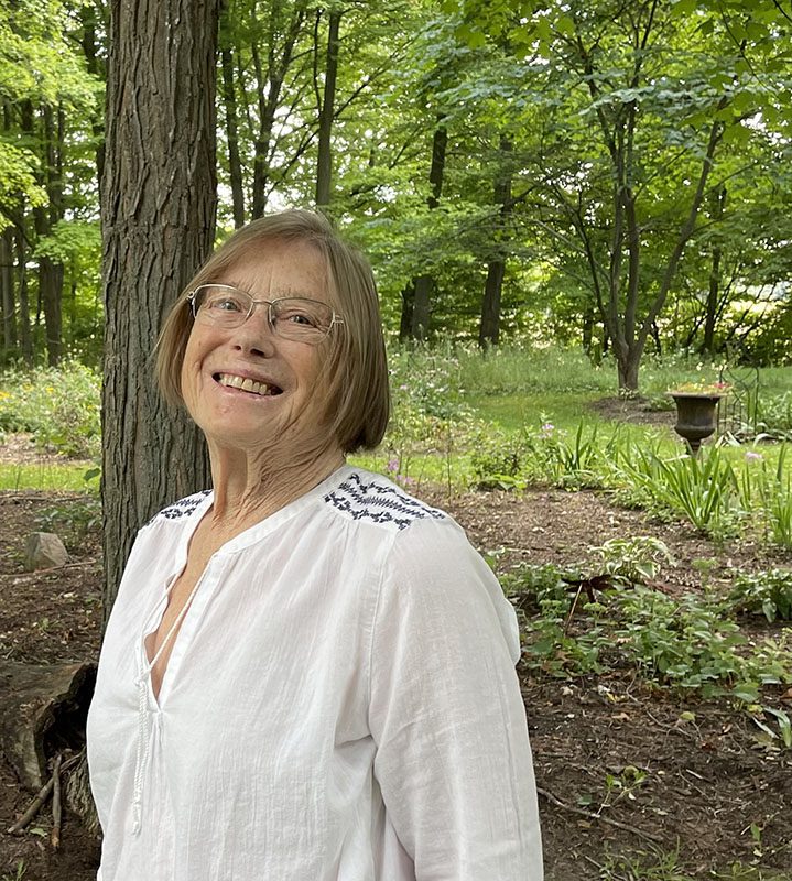 A smiling woman standing in the woods.