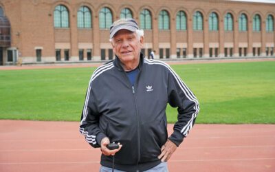 A man standing on a track field holding a stopwatch.