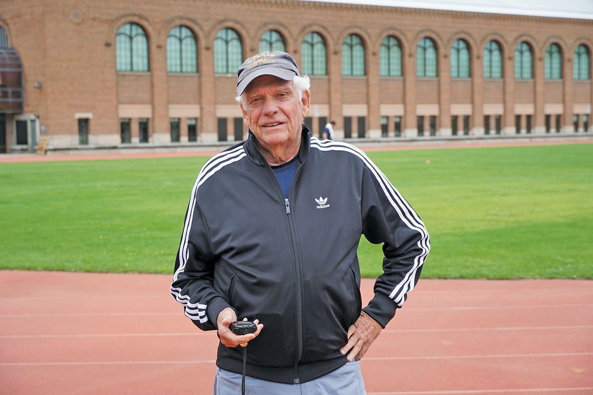 A man standing on a track field holding a stopwatch.