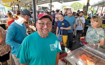 A smiling man at a crowded farmer’s market.