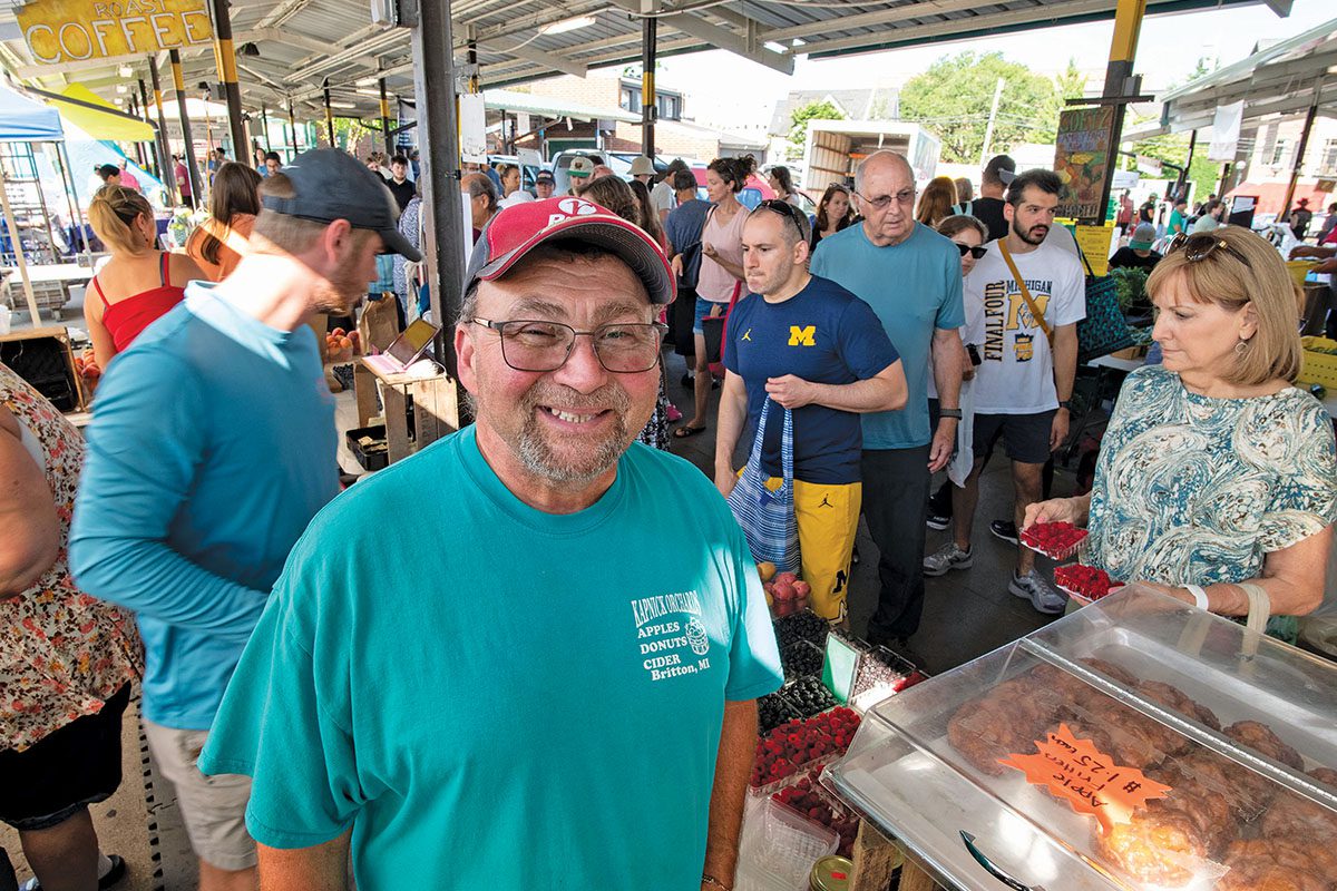 A smiling man at a crowded farmer’s market.