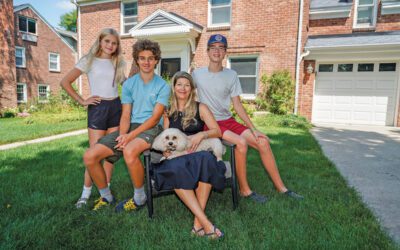 A woman holding a dog and three teenagers sitting in front of a house