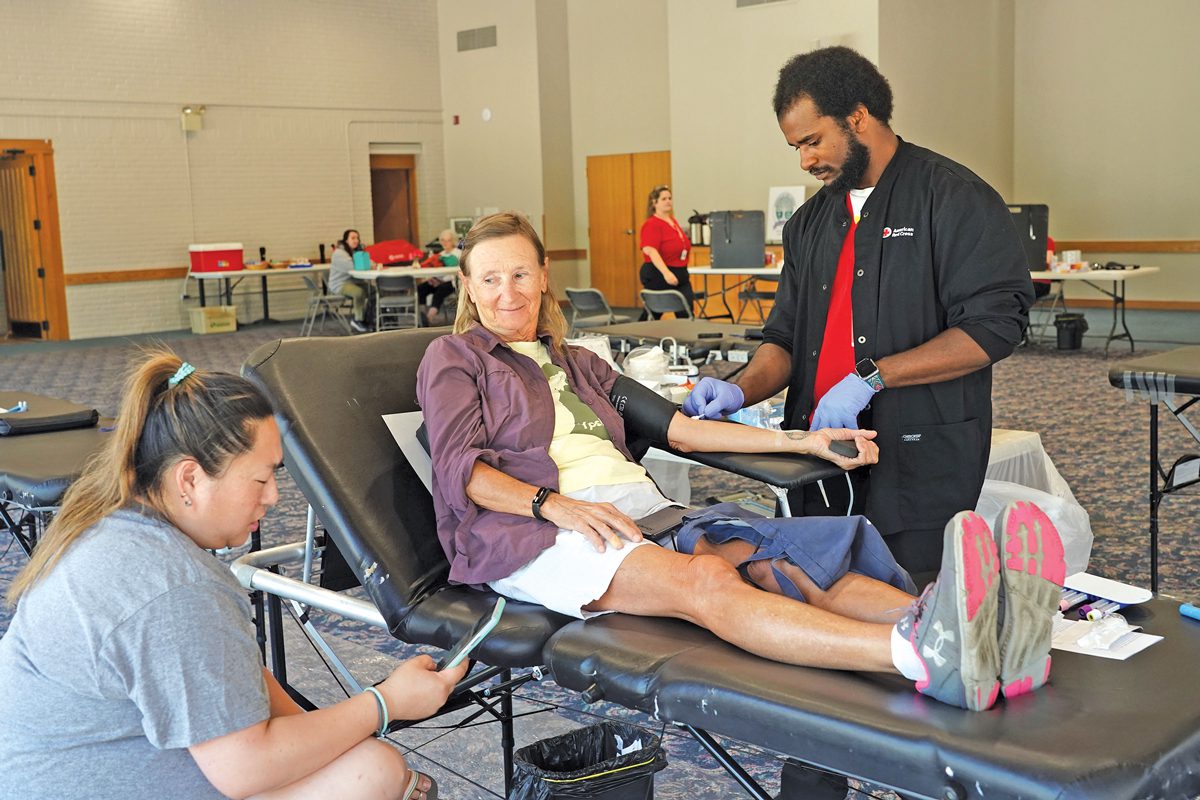 Two people assist a woman who is giving blood. 