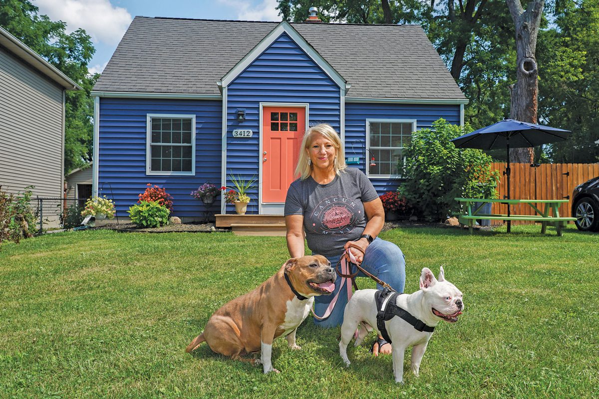 A woman in front of a blue house with two dogs