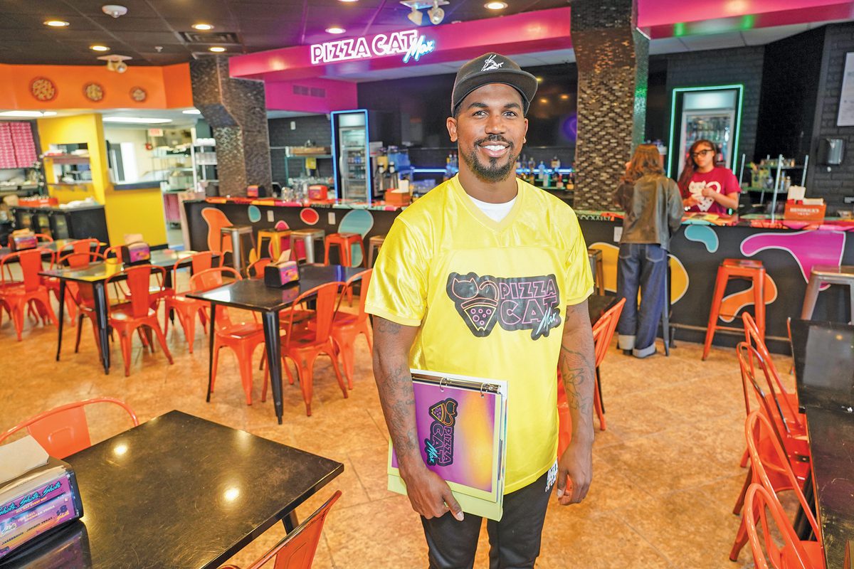 A smiling man standing in a brightly colored pizza restaurant.