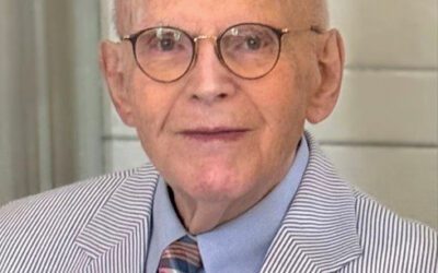 Robert Merkel wearing glasses, a collared suit, jacket, and tie