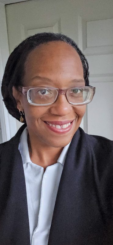 Kerene Moore smiling and wearing glasses and a dark blazer.