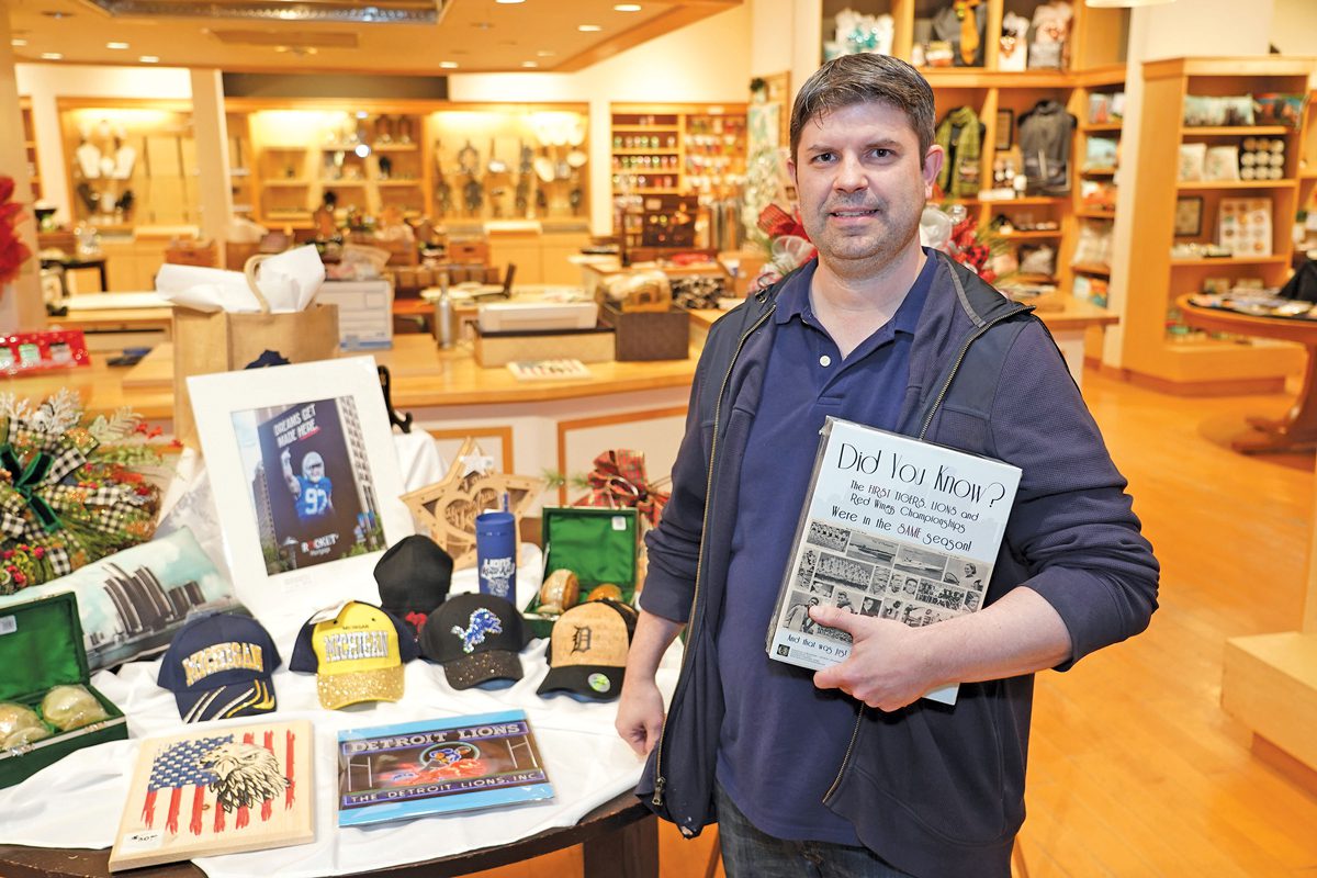 Charles Avison standing in Inspire Marketplace. He is holding a book and standing next to a table with wares for sale.