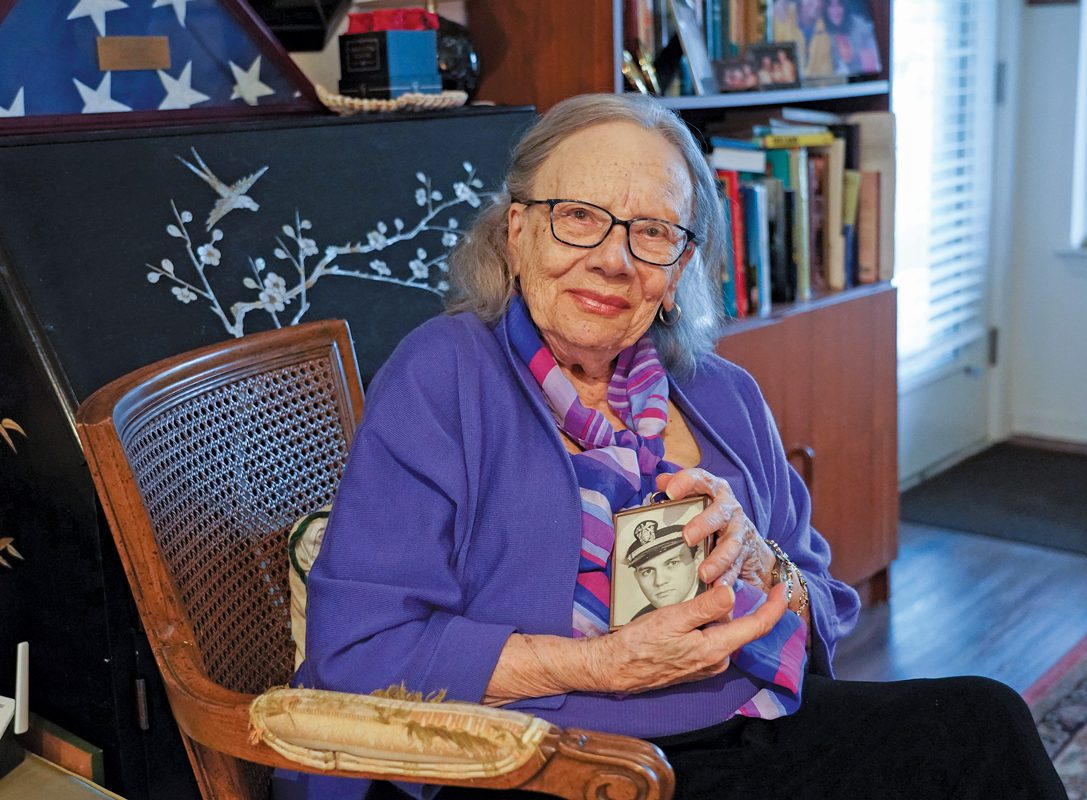 A woman wearing glasses and a purple sweatshirt and holding a framed photograph.