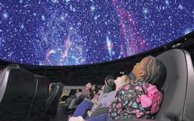 A child sitting in a planetarium and looking up at the stars above.