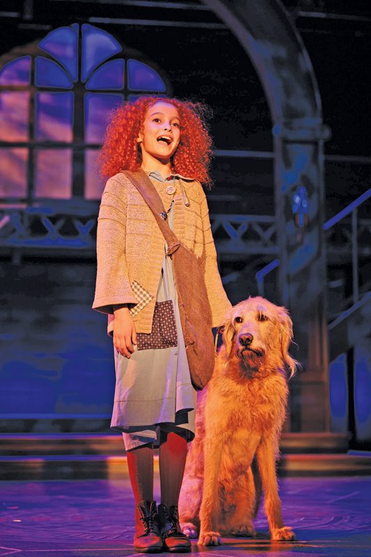 A child onstage singing next to a dog.