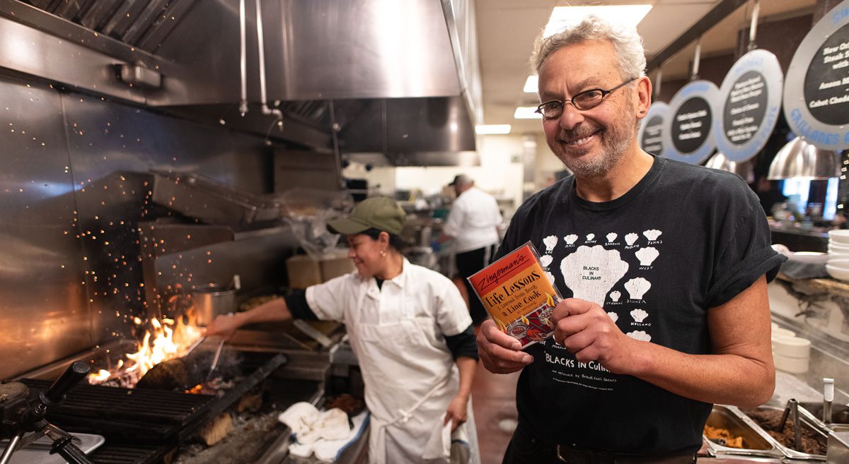 Ari Weinzweig standing in the Zingerman's kitchen holding his book.