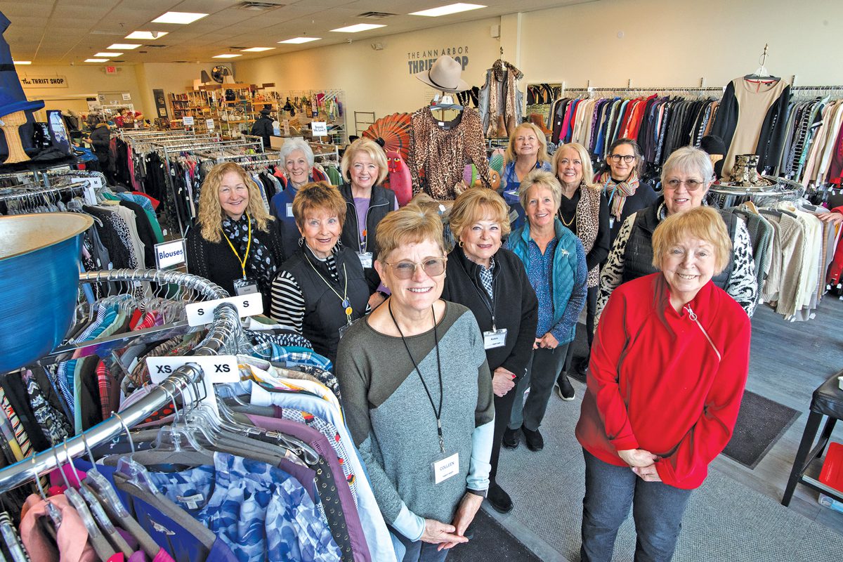 a group of 12 women standing in a thrift store filled with racks of clothing.