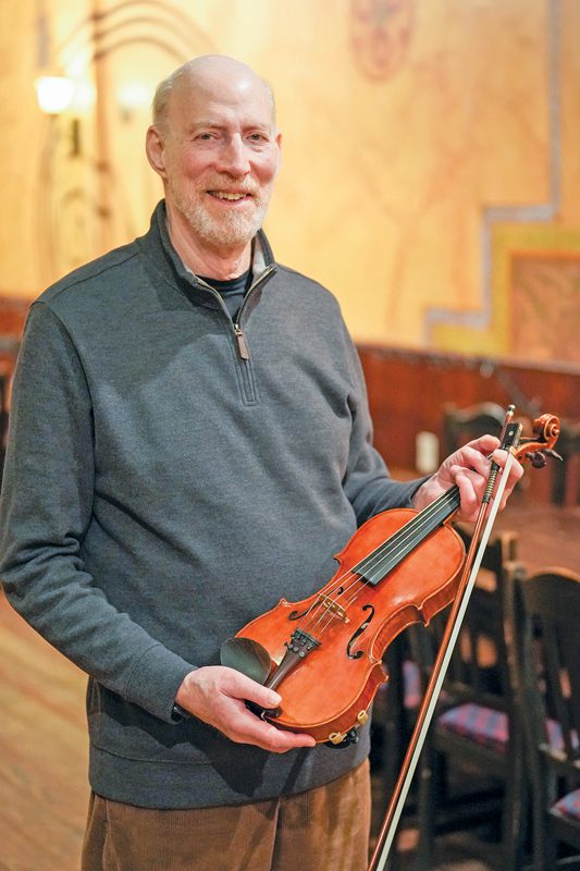 A man holding a violin in a warmly lit room.
