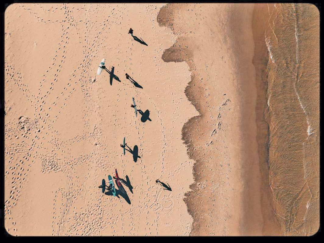 An arial shot of seven surfers walking on a beach