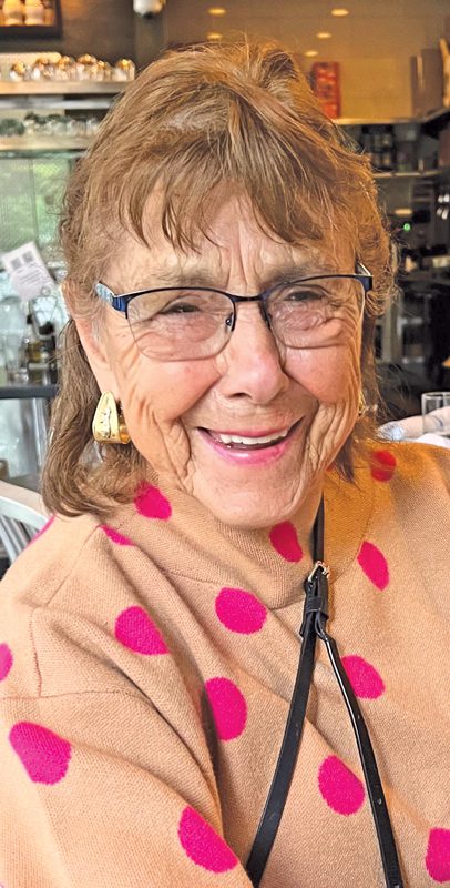 An older woman in glasses and a polka-dot sweater laughing.