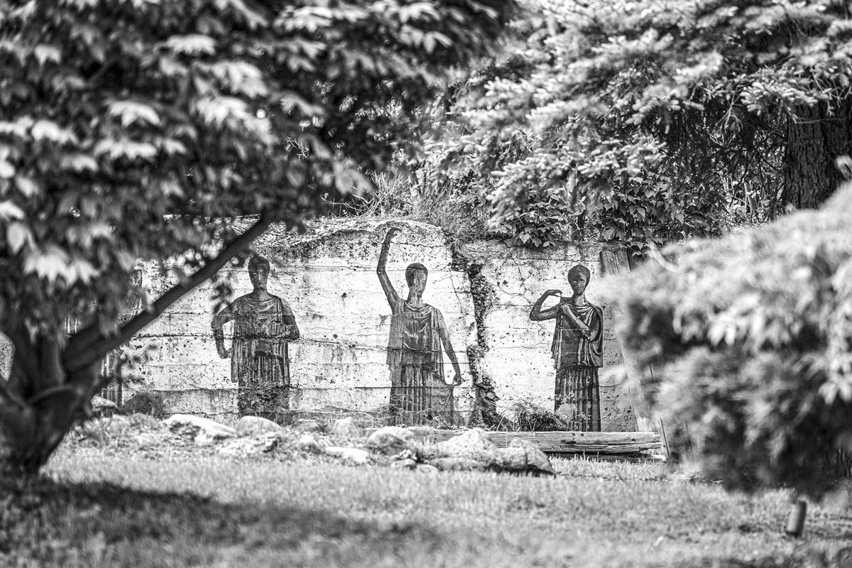 Black-and-white photo of a mural of three women. A leafy tree branch is in the foreground.