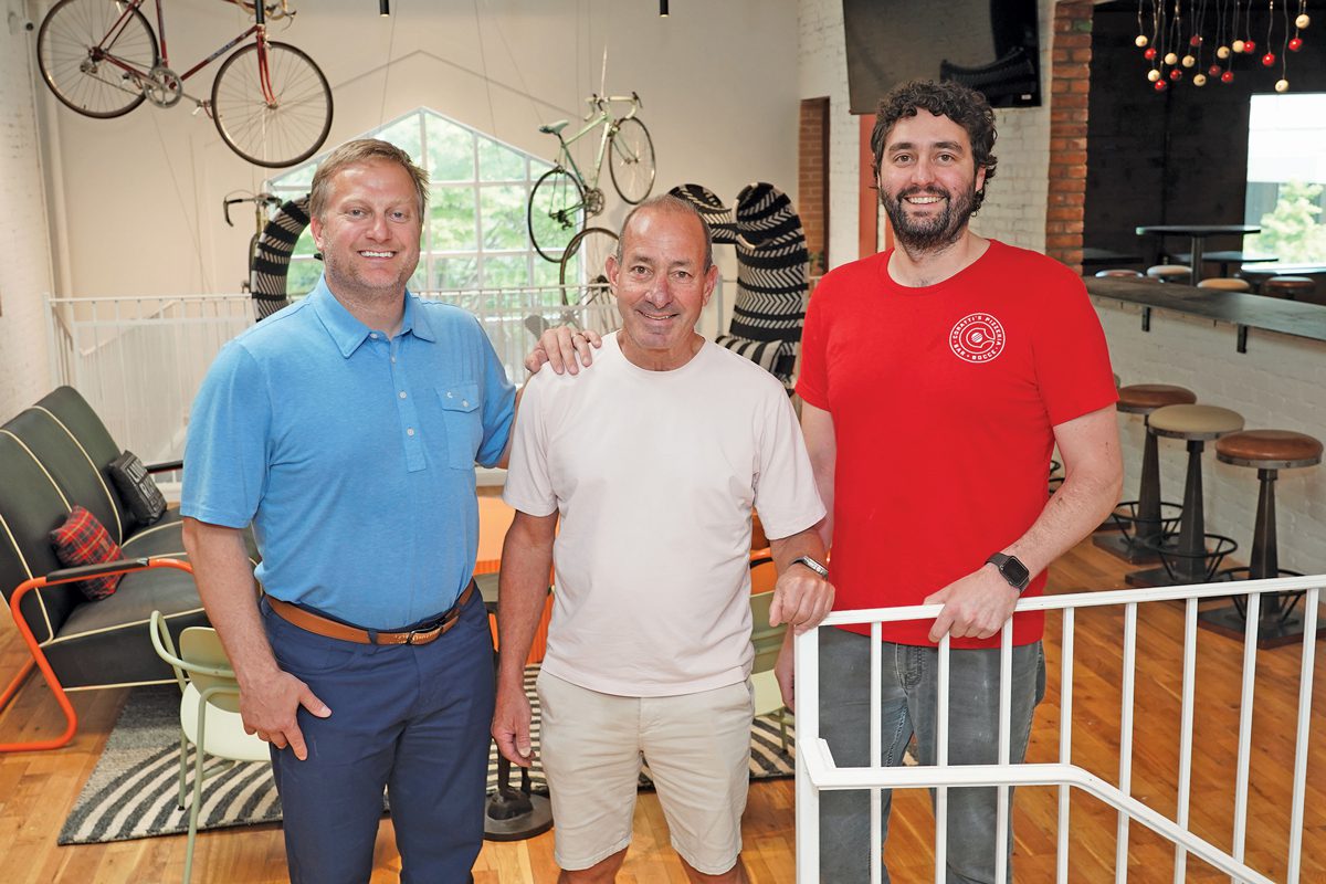 Three men standing in a bright, cheerful room. Decorative bicycles hang from the ceiling.