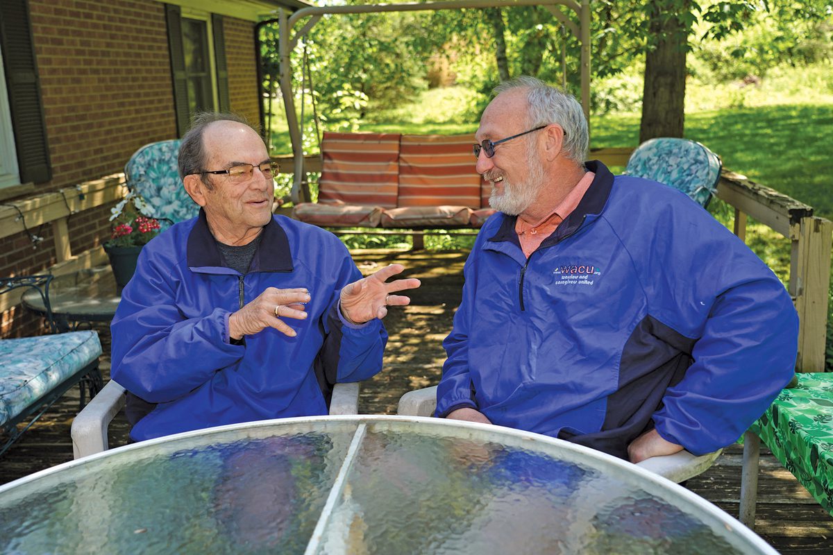 Two men sitting outside in a backyard conversing. 