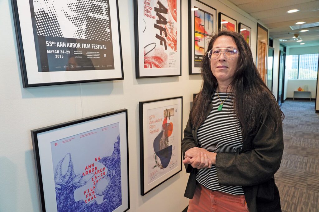 A woman stands in a hallway with posters for the Ann Arbor Film Festival. She has a worried look on her face.