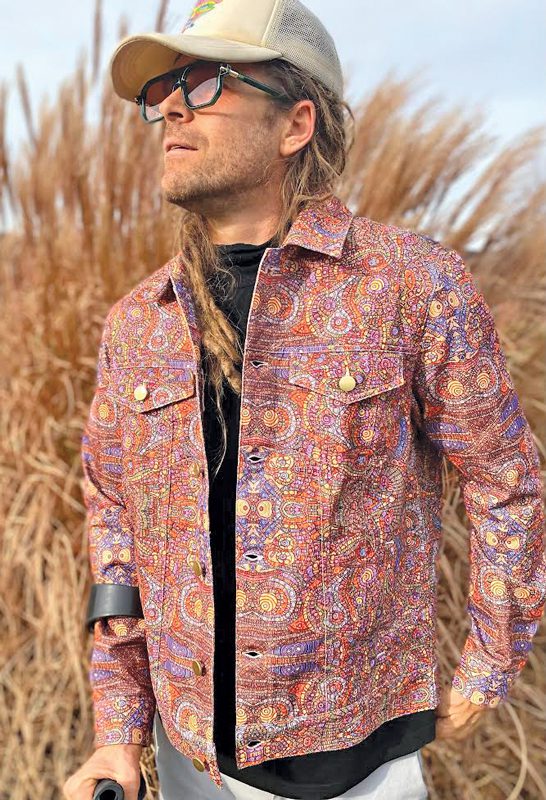 A man in an intricately detailed jacket with a pointillist pattern standing outside and looking up at the sky. 
