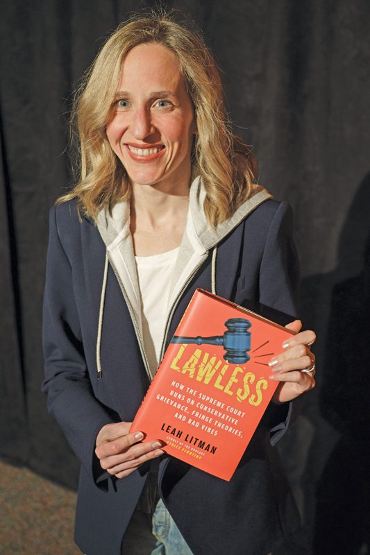 A smiling woman wearing a hooded sweatshirt with her blonde hair down. She's holding a red book titled Lawless.