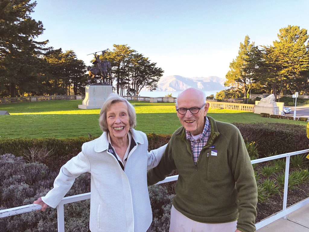 A smiling older couple standing in front of a mountain vista.