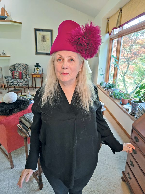 A woman wearing black with shoulder-length hair and a big pink hat with a fuzzy pom-pom on it.