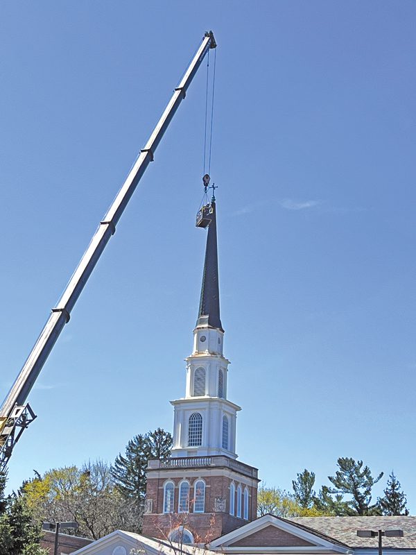 A crane getting ready to lift the spire off the steeple of a church.