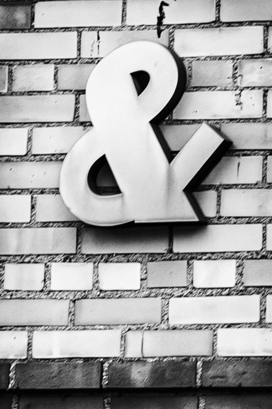 black-and-white photo of an ampersand against a brickwall
