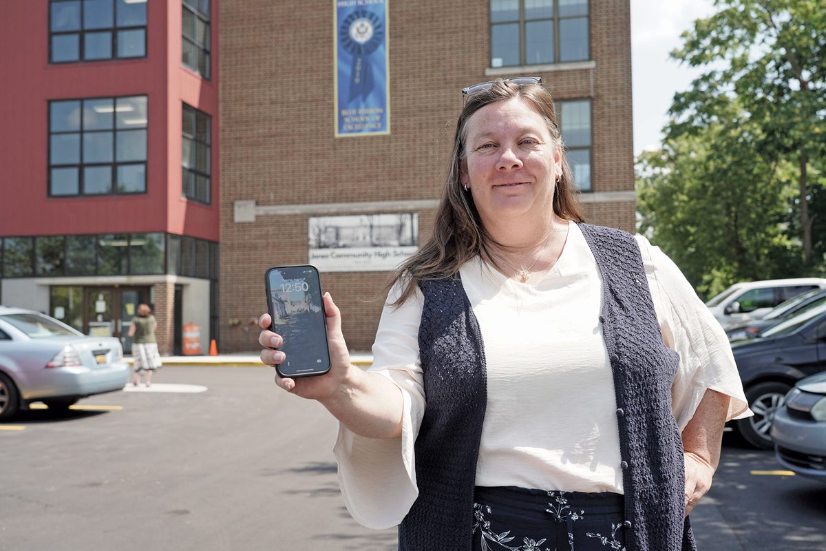 A woman stands outside a school holding a cell phone.