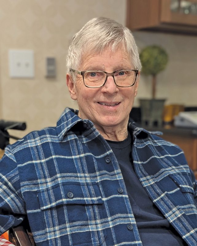 Portrait of a white-haired man with glasses and a blue flannel shirt