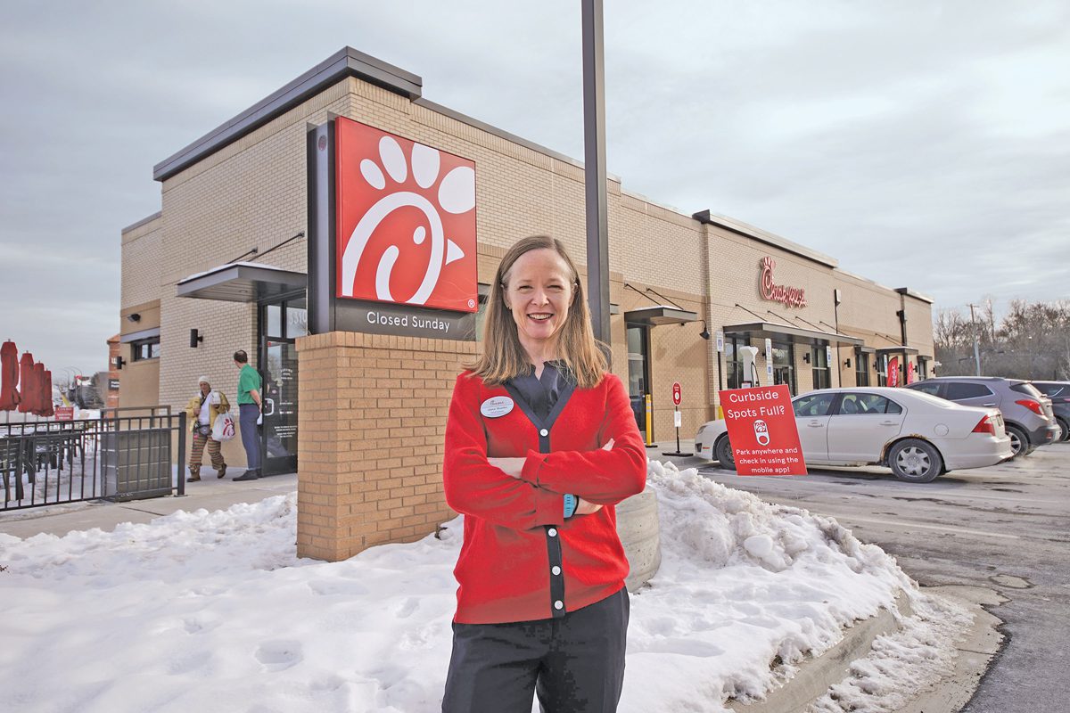 A woman stands in front of a Chick-fil-A fast food restaurant