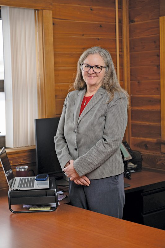 A woman stands in an office in front of a laptop.