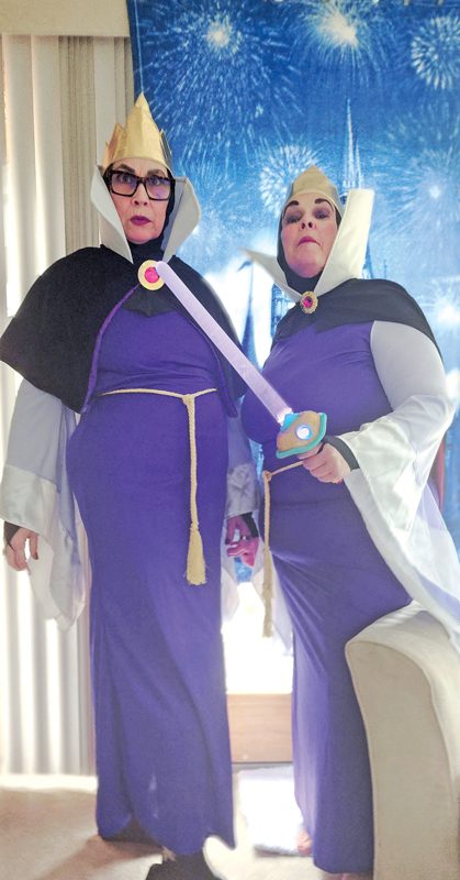 Two women dressed as evil queens in front of a Disney-themed backdrop.