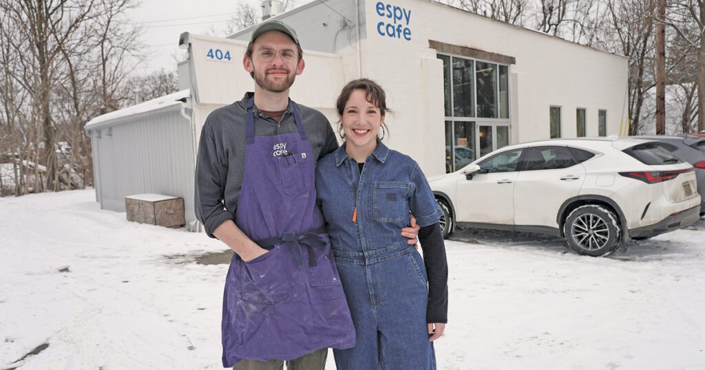 Peter Littlejohn and his wife Julia Knowles stand in front of a white building that says Espy Cafe