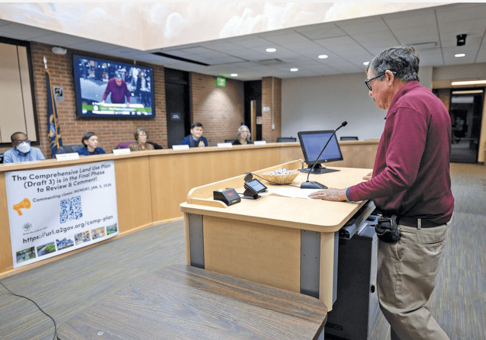 man speaking to a board at a pubic meeting