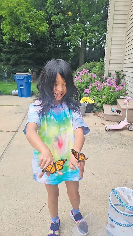 Melody Tang laughs as two monarch butterflies perch on her fingers. 
