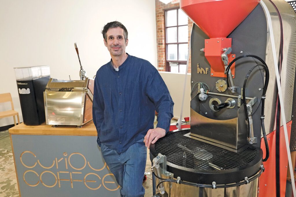 Mike Bawden stands next to a coffee roaster