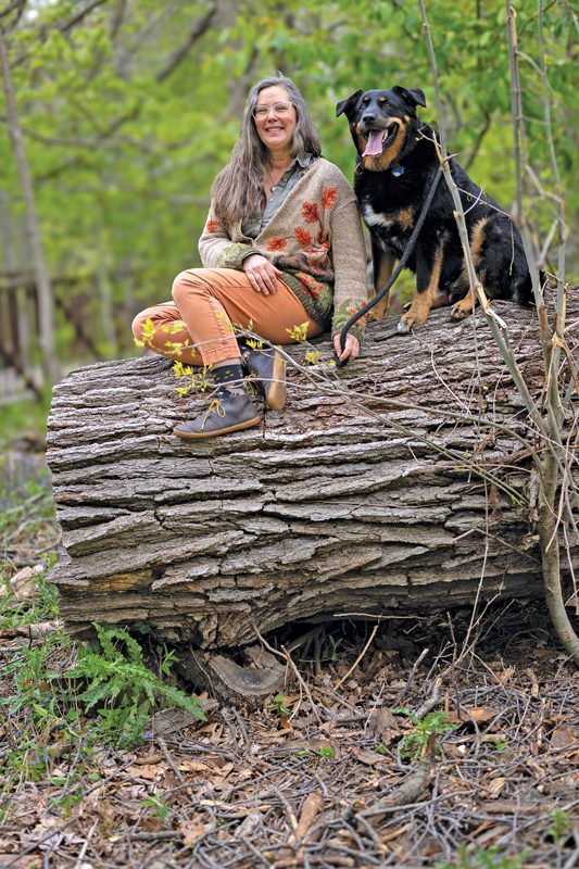 A woman and a black dog sit on a huge tree stump
