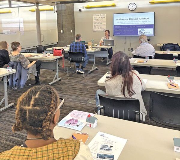 A group of people in a conference room face a PowerPoint presentation.