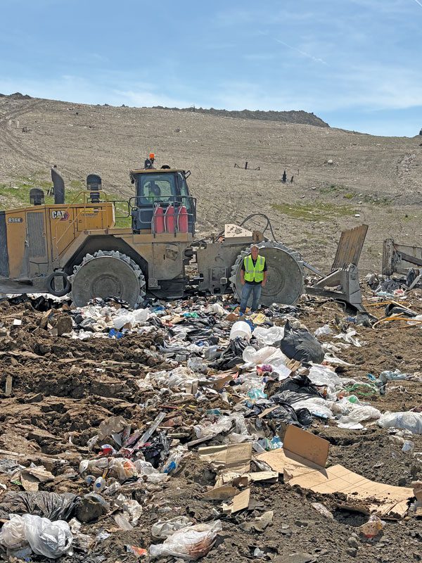 Dave Seegert stands in a landfill in front of a big machine.