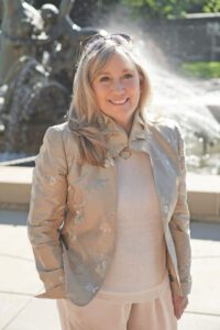 An older woman stands in front of a fountain