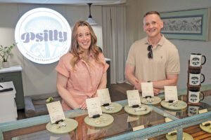 Two people stand in a shop with small plates of mushrooms in front of them