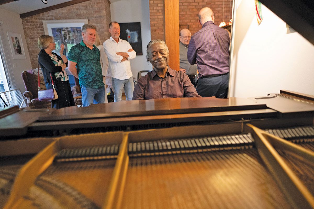 Herb Winful sits at a piano while people in the background listen.