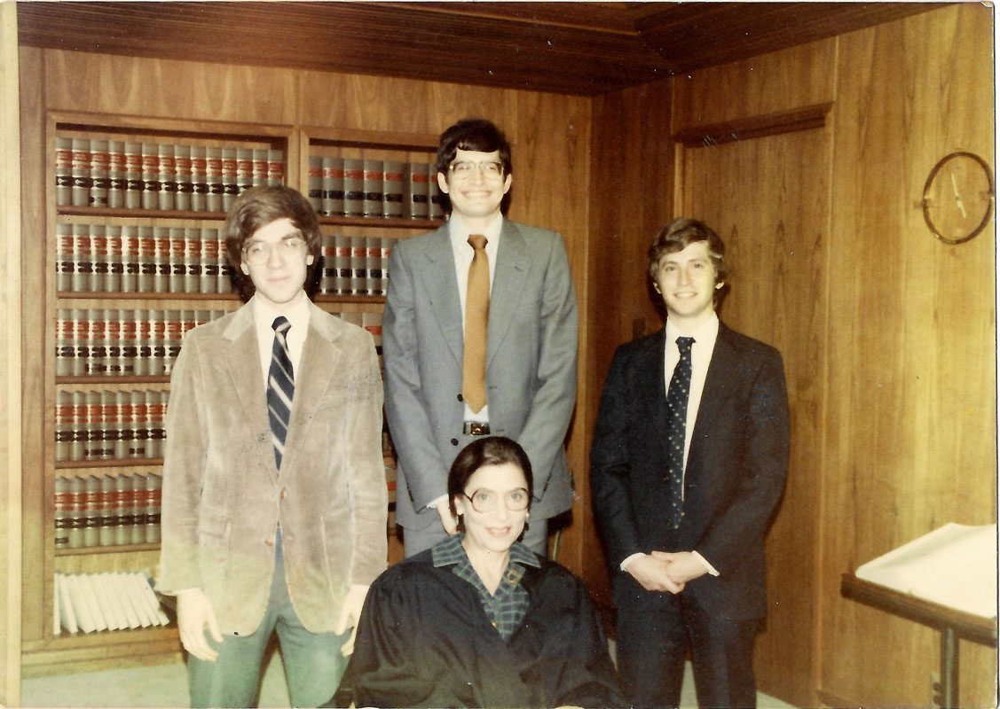 Three clerks stand behind a young Ruth Bader Ginsburg.