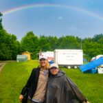 Two girls stand smiling in front of a rainbow